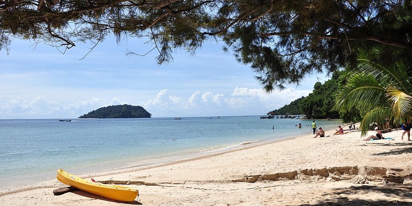An image of Manukan Island, with white sand, clear water, floating buoys, and a wooden pier