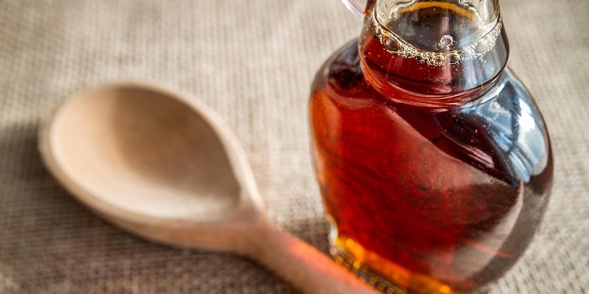 A glass bottle of rich, amber, golden-brown maple syrup to put on pancakes, waffles etc.
