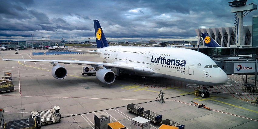 Airplane parked and connected to the passenger deck with airport buildings and vehicles