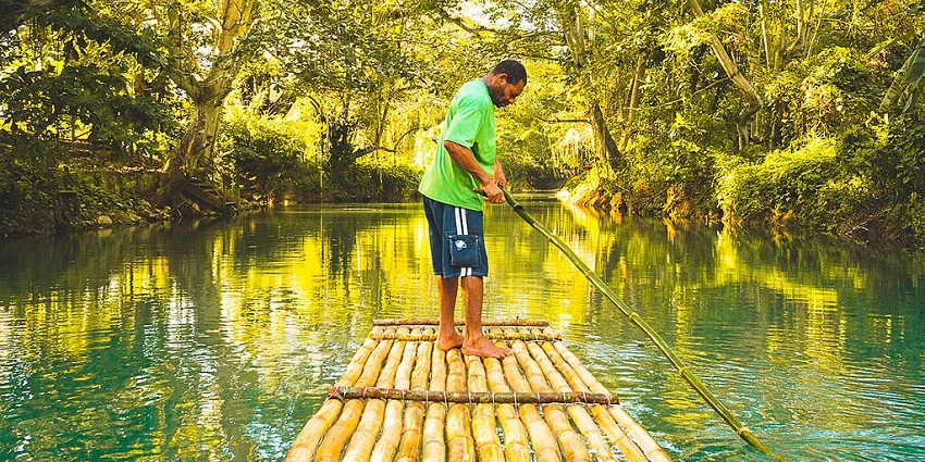 An image of a bamboo raft, with a man standing on top, floating on the Martha Brae river, one of the great places to visit in Falmouth.