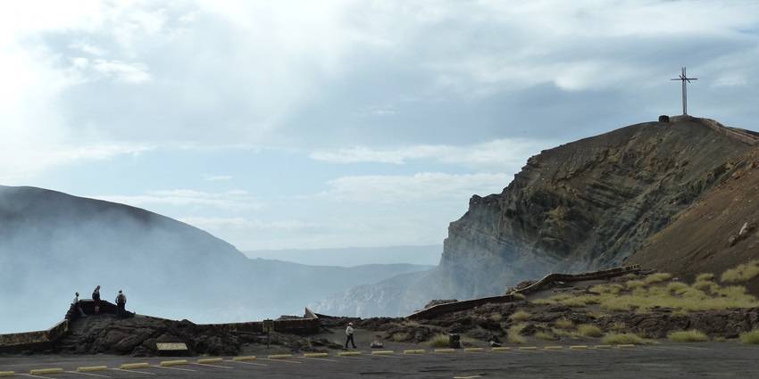 Masaya Volcano emits smoke from its crater, with rugged slopes and a cloudy sky above.