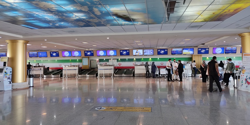 Modern interior of Mashhad Airport, with people wearing masks and standing in groups.