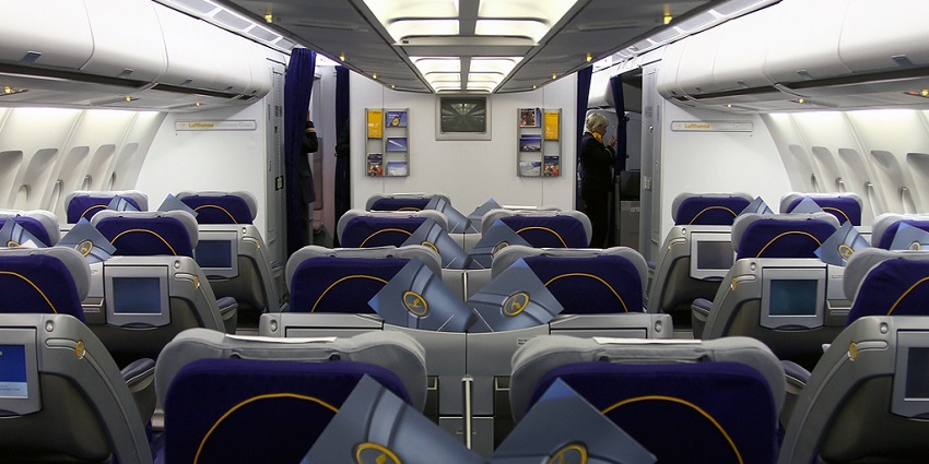 Inside an aeroplane in business class with empty seats and a person standing in a corner