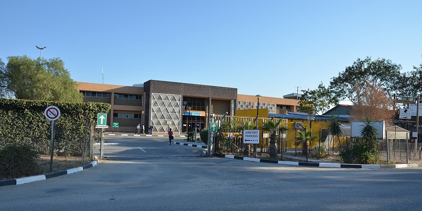 A person is walking towards the airport entrance while others are standing near the building.