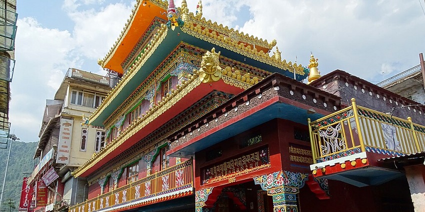 An image of a colorful, multi-tiered Buddhist temple in McLed Ganj, with intricate architectural details, decorations, and vibrant colors.
