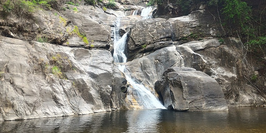 Meenmutty waterfalls flowing into a small pond with low pressure from the rocky surface