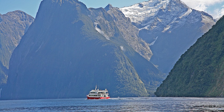 An image of a ferry boat on waters in Milford Sound, surrounded snow-capped mountains.
