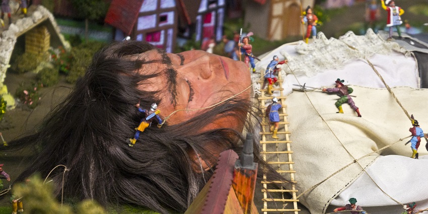 An image of Gulliver restrained on the ground by Lilliputians using ropes, ladders, and historical attire at the Miniature World, Victoria.