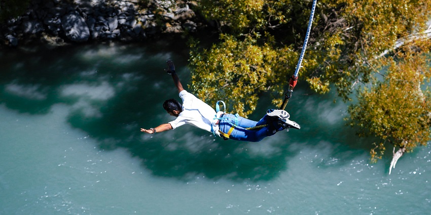 A person mid-air during bunjee jumping in South Goa, suspended upside down with a securely fastened harness against a bright blue sky.
