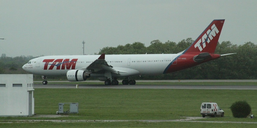 Airbus A330 aeroplane on the runway with red tail and a car parked near the runway