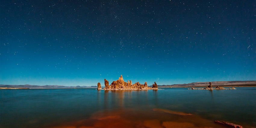 Mono Lake’s tufa towers above crystal blue waters under a sky full of stars at pitch blue night