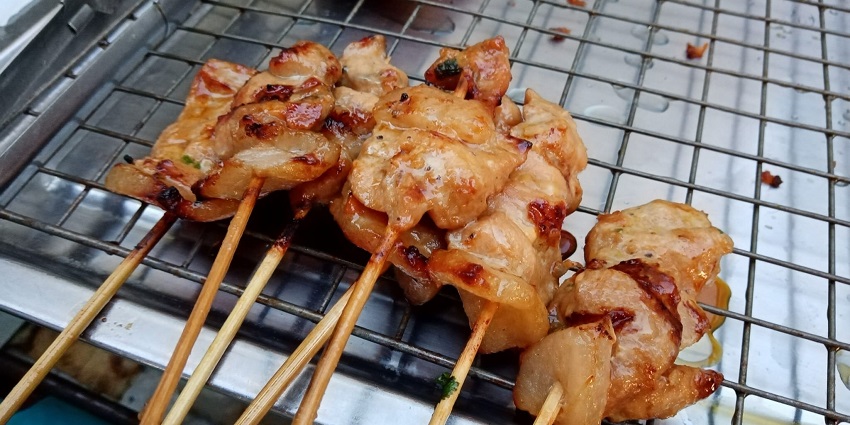 Grilled Moo Ping pork skewers, a flavorful Thai street food, served with sticky rice and sauce