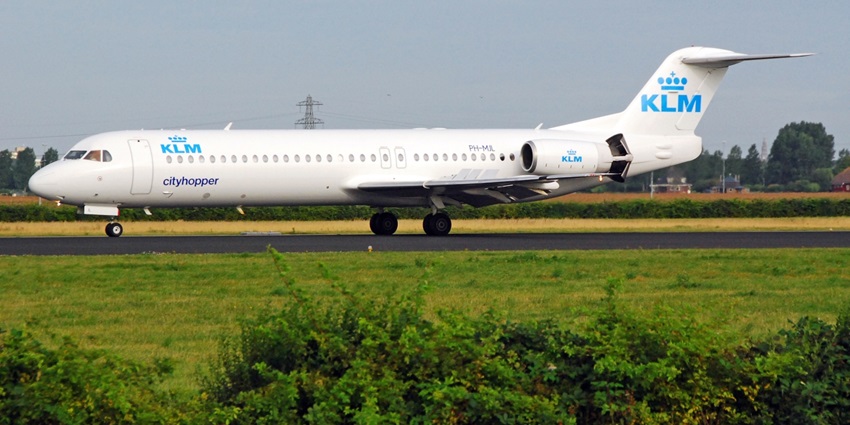 Blue and white commercial aeroplane on the runway of an airport with green trees and plains