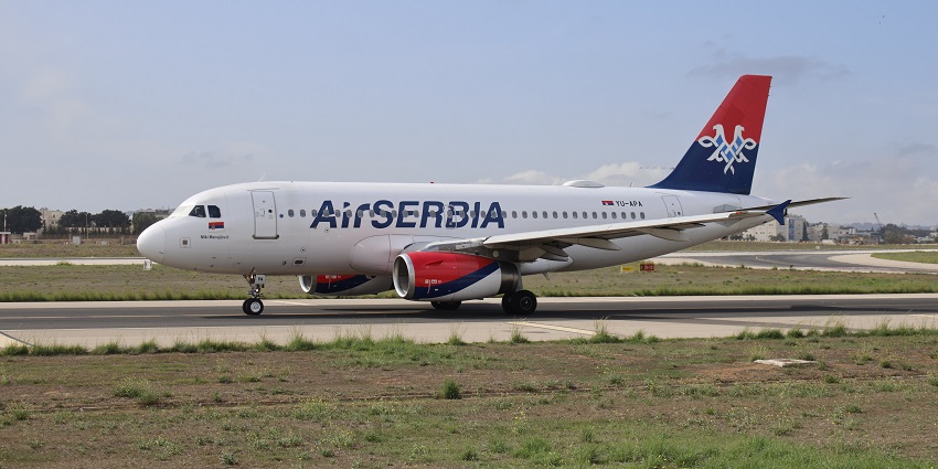 An aeroplane parked on a runway at the airport with red and blue tails and green plains