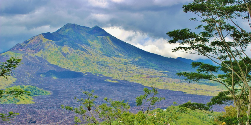 Mount Batur’s majestic peak rises above lush greenery and dark lava fields in Bali.