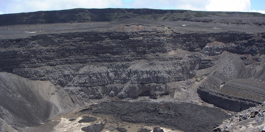 Mountain Karthala volcano surrounded by black sandy cliffs and stones under a blue sky