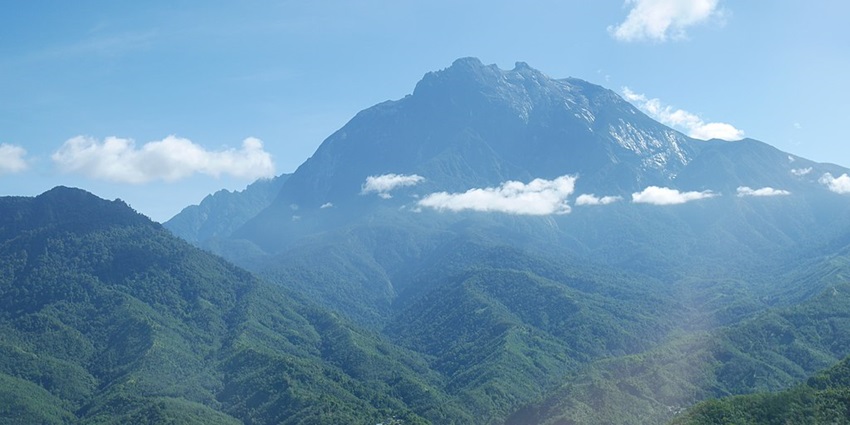 An image of Mount Kinabalu partially veiled by clouds, with a village visible below
