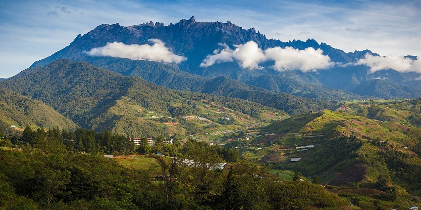 A morning view of Mount Kinabalu with clouds witnessed from lush green plains of Borneo.