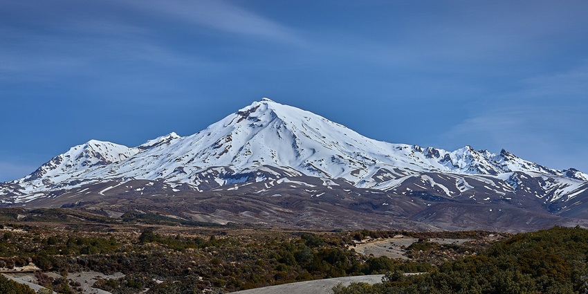 A scenic view of Mount Ruapehu, a towering active volcano near Tawhai Falls in New Zealand.