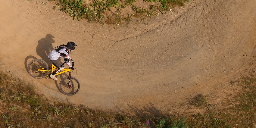 Person mountain biking on a yellow bicycle while wearing safety gears on a sandy, dirt road
