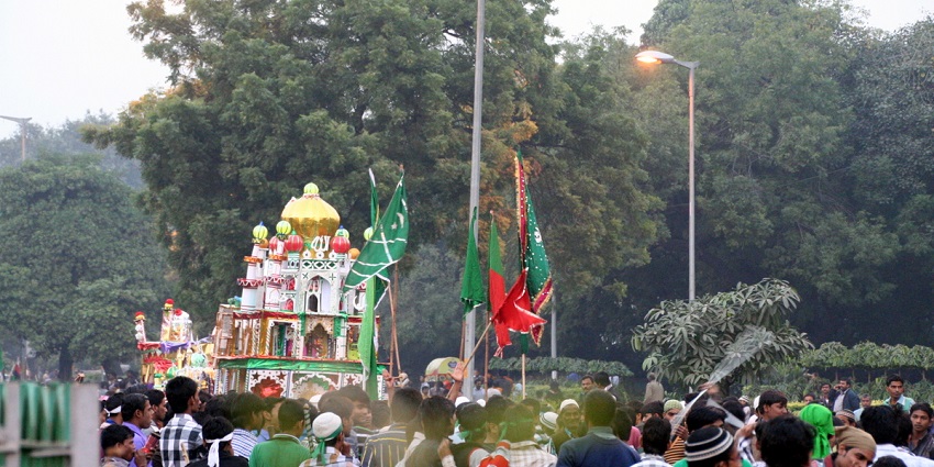 An image of a large gathering of people around ornate structures, engaged in a cultural procession during the Muharram festival.