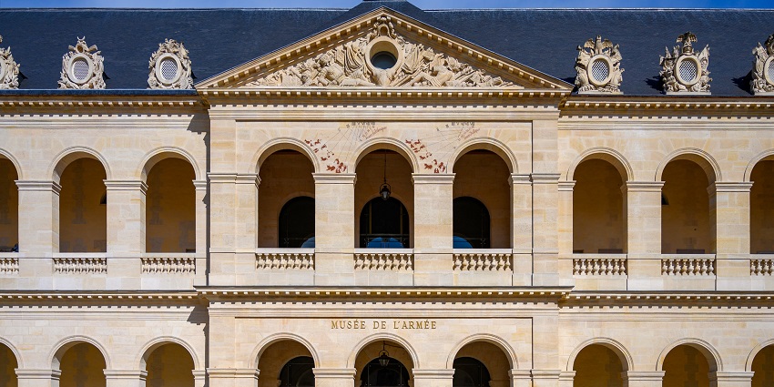An image of Musée de l'Armée Paris, showcasing classical arches, columns, text, cannons, and visitors.
