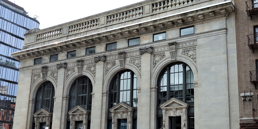 An image of the Museum of Illusions building in New York, with large columns, banners, and people walking nearby.