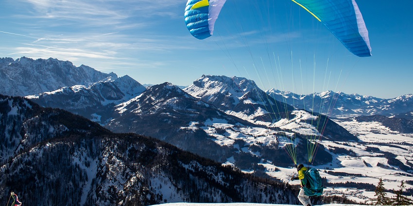 A paraglider launching from a snowy mountain with a stunning view of snow-covered peaks.