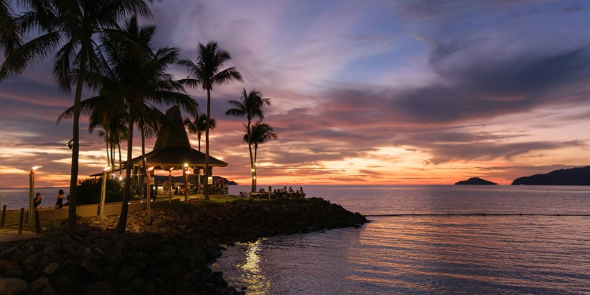 An image of a coastal area of Kota Kinabalu during sunset, featuring anchored boats and calm waters