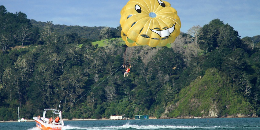 Parasailing over the water with a colourful parachute, soaring high above the sea with a speedboat towing the rider.