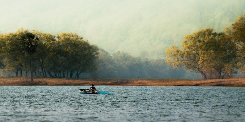 A picture of a serene lake with a kayak amidst a misty forest, resembling lakes in India.