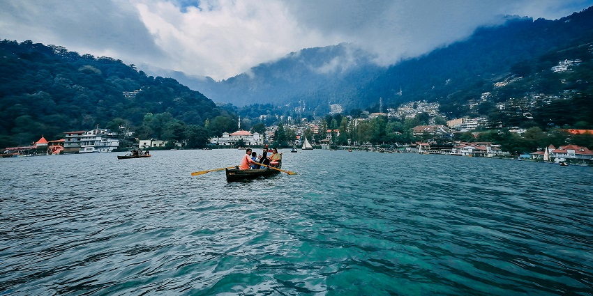 An image of a calm lake in Nainital, surrounded by green hills with a town located on the slopes, one of the most famous hill stations in India to visit in September.