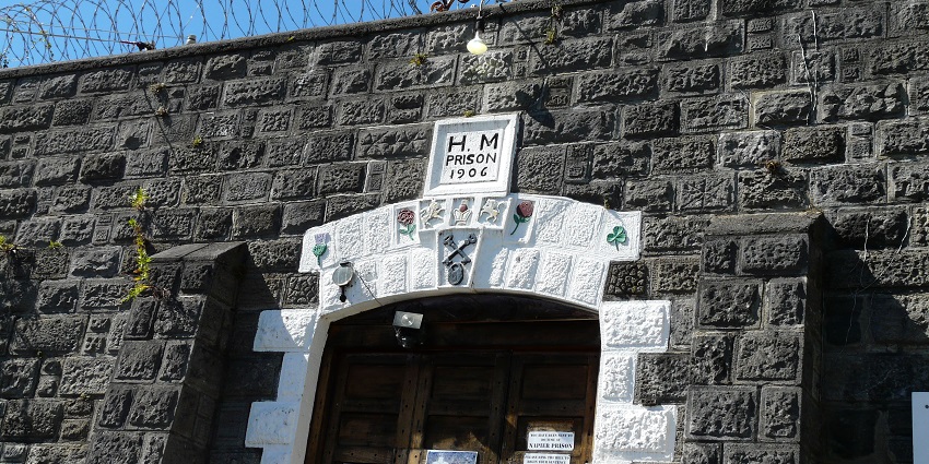 Entrance to the Napier Prison featuring dark stone walls, barbed wire, and white-framed decorative details.