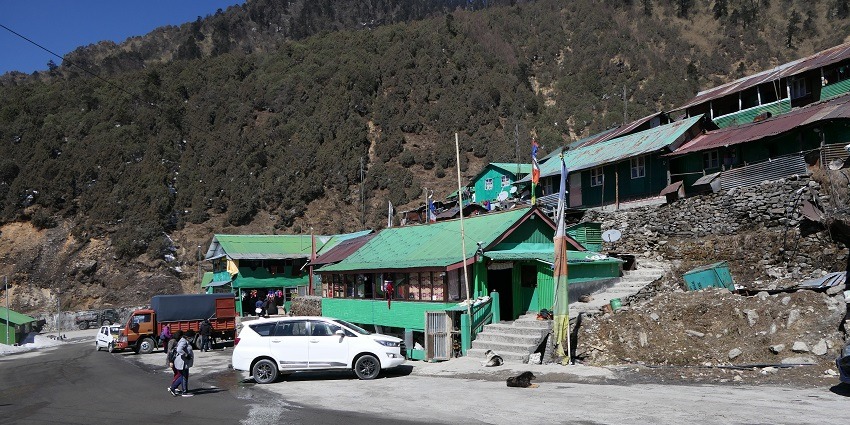 Nathula pass with a road, buildings, multiple vehicles parked, people standing and mountains.