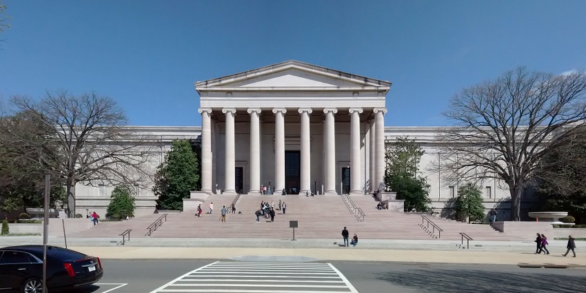 Front view of the National Gallery of Art in Washington D.C. during the day, showing its neoclassical columns and wide staircase under a bright blue sky.