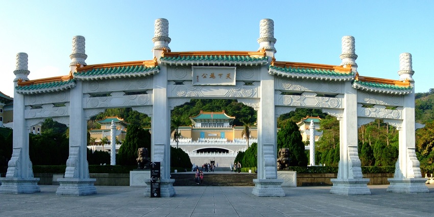 Daytime view of the National Palace Museum in Taipei featuring its traditional Chinese-style roof and green hills in the background under a clear sky.