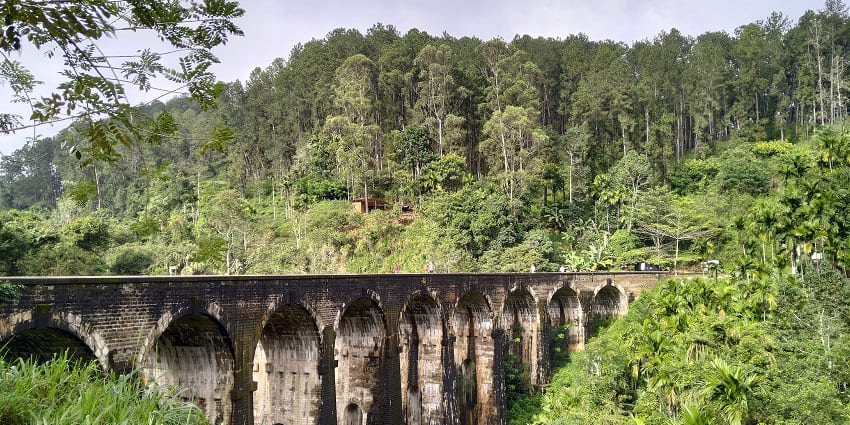 A picture of a historical overwater bridge in Sri Lanka with nine arches, surrounded by lush greenery
