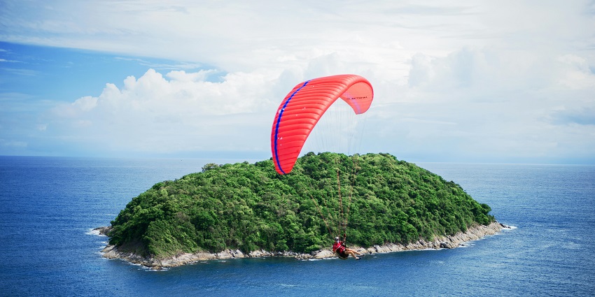 A person with a red parachute glides toward the water, moments away from a smooth landing
