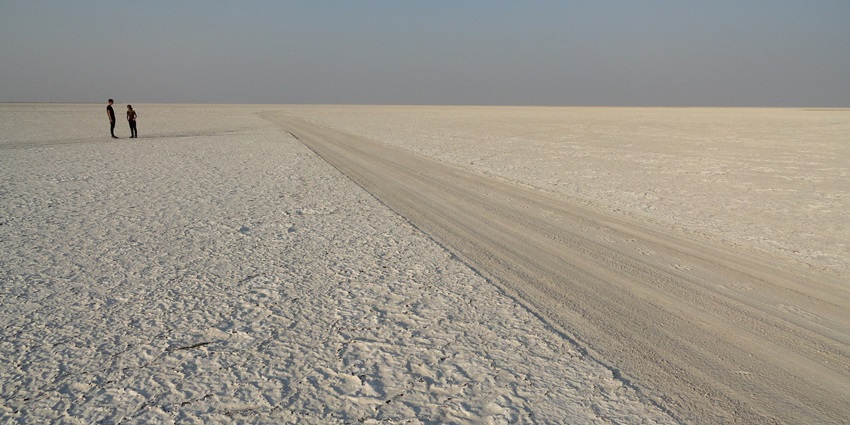 Ntwetwe pan in Botswana with marks making a trail, two men standing in the desert