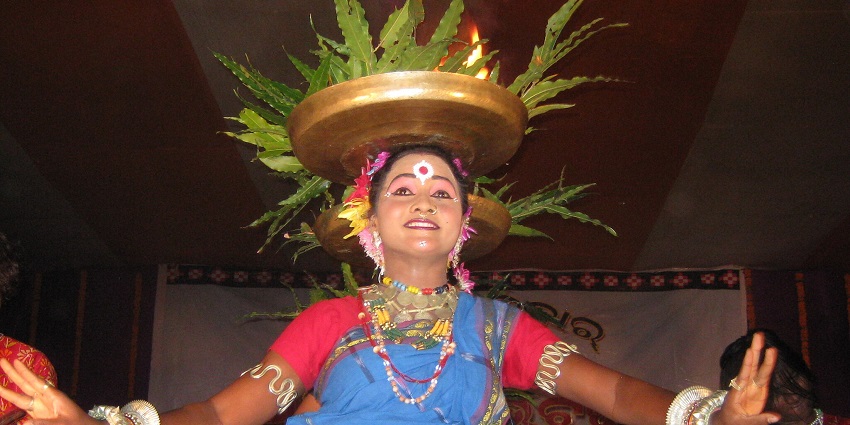An image of a cultural dance performance of Nuakhai festival, with people in traditional attire, holding plates with green leaves.