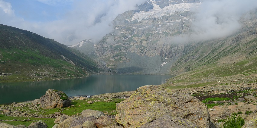 Nundkol lake with a blue water body, rocky shorelines and mountain peaks covered in snow