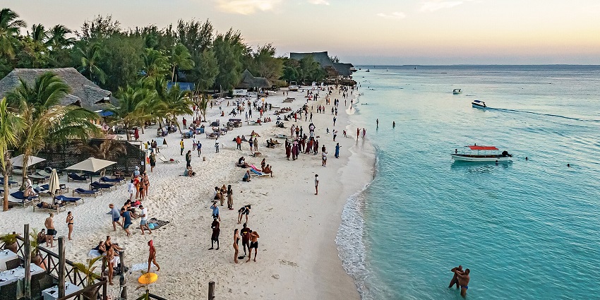 Tourists stroll along Nungwi Beach, one of the most beautiful beaches in Africa, soft sand as the sun sets over the horizon.