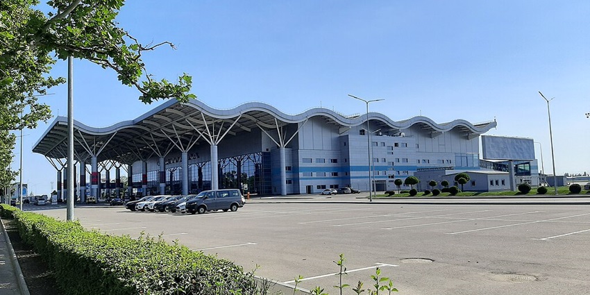 Odesa Airport's modern grand architecture, parked cars, and lush green gardens under a clear sky