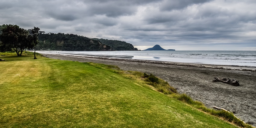 A scenic view of Ohope Beach with golden sand and gentle waves along the coastline.