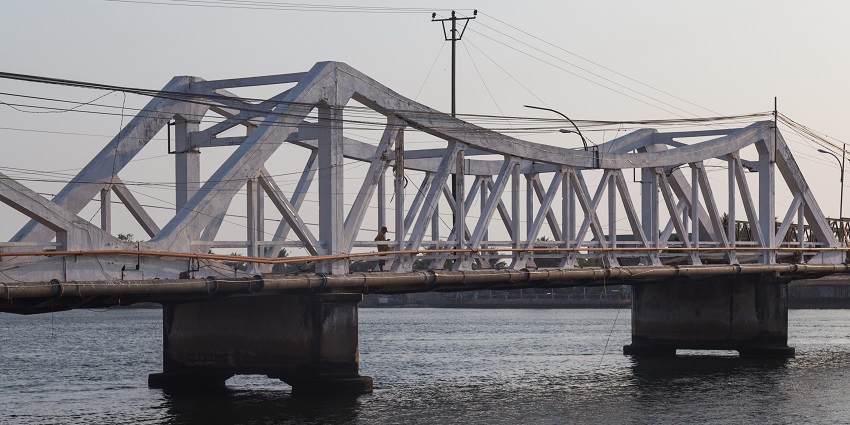 An image of an old bridge in Kampot, Cambodia, with a weathered structure and river views.