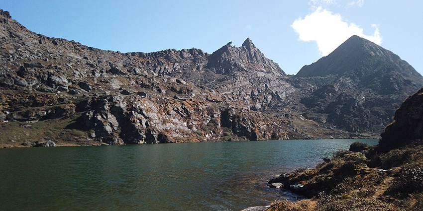 A serene lake in Bhutan with still waters reflecting rugged mountain peaks under clear skies