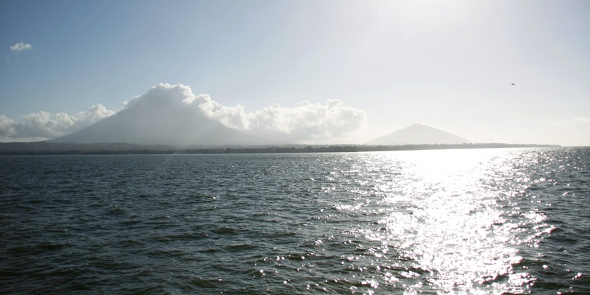 Ometepe Island appears in the distance, surrounded by calm waters under a blue sky.