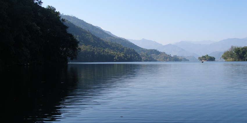 Fewa Lake with a large and still water body surrounded by greenery and mountains