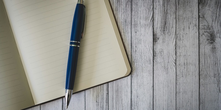 A lined notebook with a sleek blue pen resting on it, placed on a rustic wooden surface