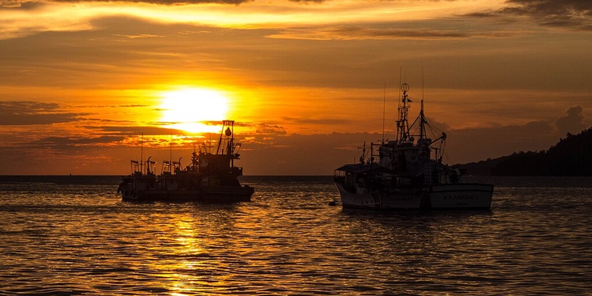 An image of a serene sunset in Kota Kinabalu, with two silhouetted boats and golden reflections